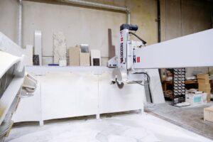 Fabricator cuts a stone slab beside polished countertop sections with sink and cooktop openings.