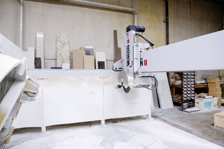 Fabricator cuts a stone slab beside polished countertop sections with sink and cooktop openings.